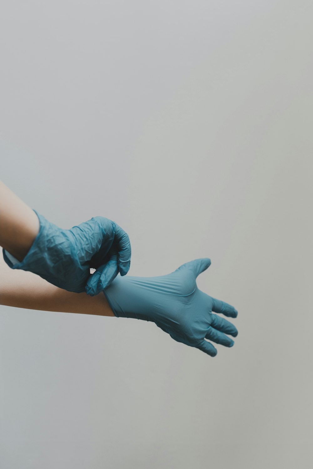 A hand in a blue nitrile glove held out against a grey wall